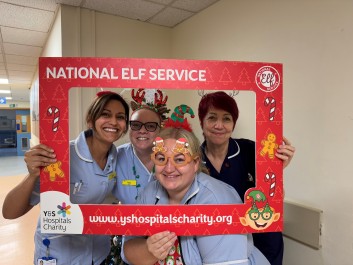 Staff dressed in festive attire, smiling and holding charity logo board