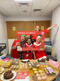 Staff dressed in festive clothing smiling with charity logo board