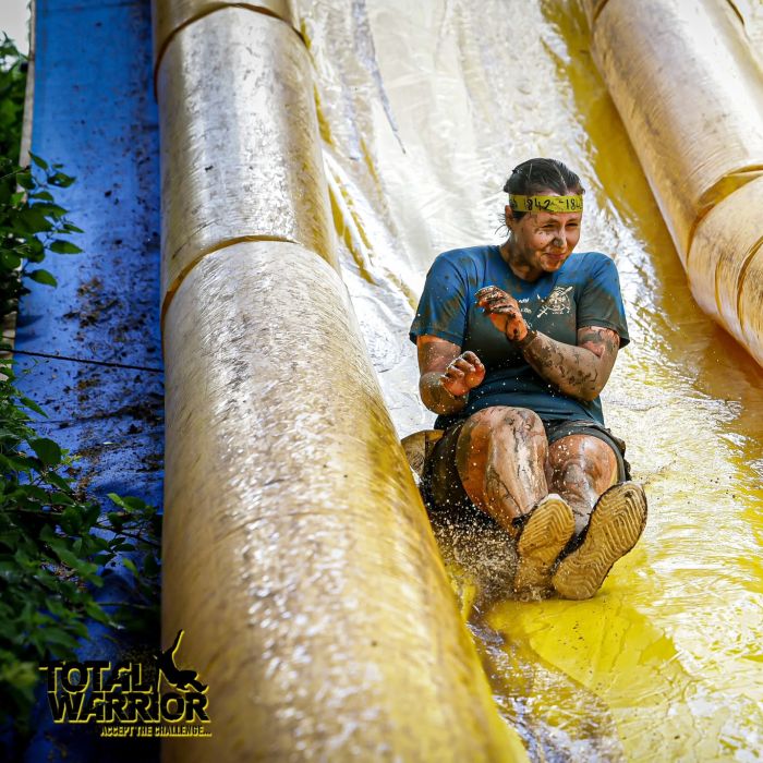 Lady covered in mud going down an inflatable slide 