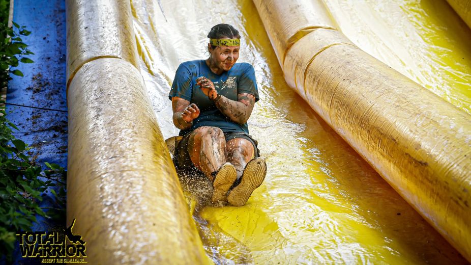 Lady covered in mud going down an inflatable slide 
