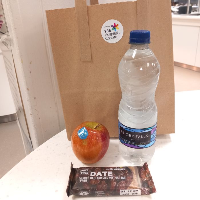Brown paper bag with charity logo, an apple, bottle of water and date bar