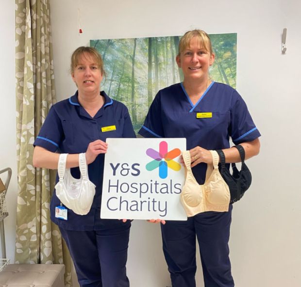 two staff members hold bras and charity logo